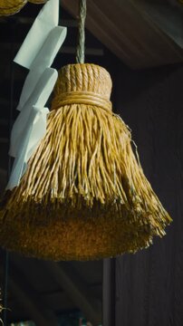 cinematic vertical close-up shot panning right on traditional japanese shinto shimenawa straw ropes and white shide paper streamers at a shrine