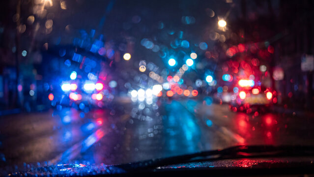 Vibrant emergency vehicle lights reflecting on wet windshield during heavy nighttime rainstorm with colorful blurred city bokeh