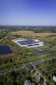 Aerial view of a data center facility with solar panels on the roof, surrounded by green lawns, a small pond, and autumn trees in Volo, Illinois, United States.