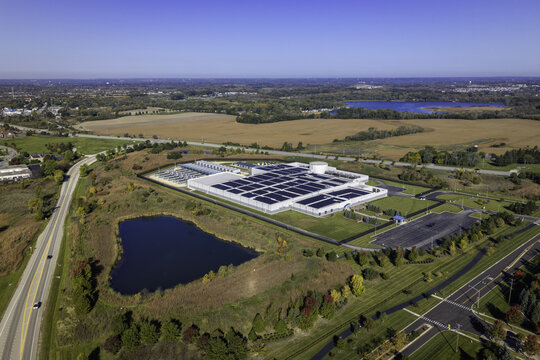 Aerial view of a data center facility with rooftop solar panels, surrounded by autumn foliage, a small pond, and rural landscape in Volo, Illinois, United States.