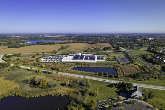 Aerial view of a large data center facility with rooftop solar panels surrounded by autumn fields, ponds, and roads in Volo, Illinois, United States.