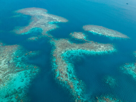 Aerial view of a vibrant coral reef surrounded by deep blue ocean waters in Karimunjawa, Central Java, Indonesia.