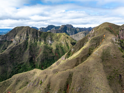Aerial view of Codo de los Andes, showcasing rugged mountain ridges, grassy slopes, and deep valleys under a cloudy sky in Samaipata, Santa Cruz Department, Bolivia.