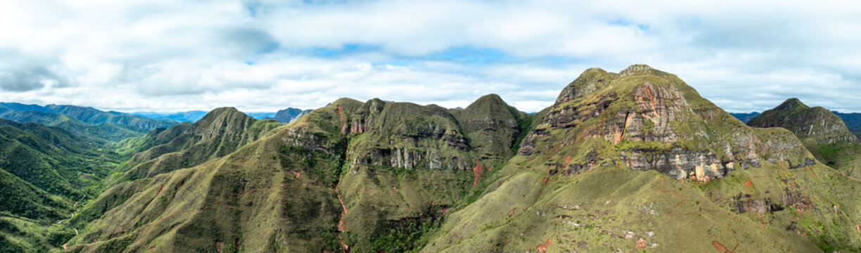 Aerial view of the Codo de los Andes mountain range featuring rugged green slopes, rocky cliffs, and deep valleys under a cloudy sky in Samaipata, Santa Cruz Department, Bolivia.