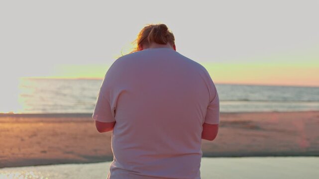 Back view of a person watching the sunset over the ocean from a quiet sandy beach shoreline