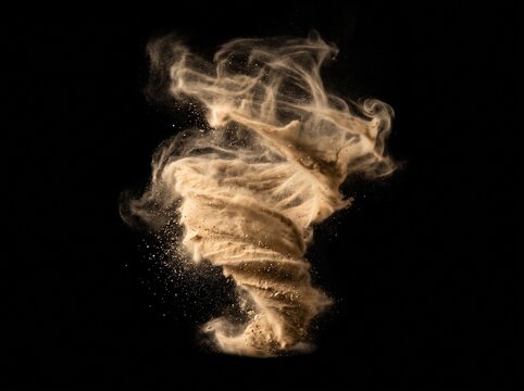 Dynamic swirling vortex of fine brown sand and dust particles forming a twisting tornado shape with wispy smoke trails isolated against a solid dark black background