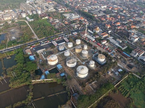 Aerial view of PT Pertamina Terminal BBM Sanggaran with industrial fuel storage tanks, surrounded by urban buildings and roads in Kecamatan Denpasar Selatan, Bali, Indonesia.