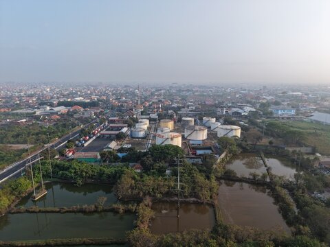 Aerial view of PT Pertamina Terminal BBM Sanggaran with large fuel storage tanks, industrial infrastructure, fish ponds, and urban sprawl in Kecamatan Denpasar Selatan, Bali, Indonesia.