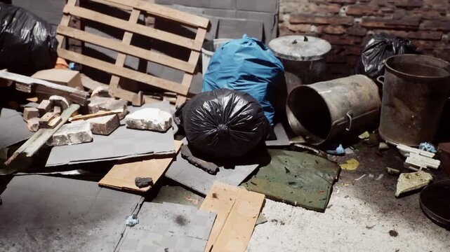 Trash and construction waste sit near pallets and metal containers in a dim, brick walled urban alley, with natural daylight casting shadows.