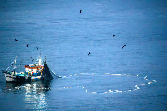 Aerial view of a fishing boat casting nets into the deep blue ocean with seabirds flying overhead in Rio de Janeiro, Rio de Janeiro, Brazil.
