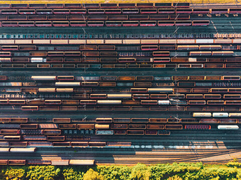 Aerial view of a large wagon depot with numerous freight train cars parked on parallel tracks near a forest edge in Czechia.