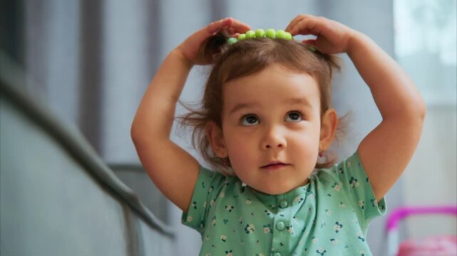 Cute toddler plays with colorful beads. Her pigtails bounce as she smiles. Bright beads catch soft indoor light. Child enjoys simple toy with pure delight. Perfect for parenting, baby