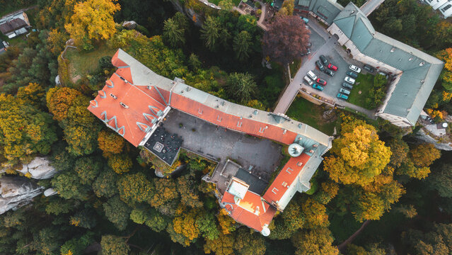 Aerial view of Zamek Hruba Skala surrounded by colorful autumn trees and rocky terrain in the evening light, Hruba Skala, Liberec Region, Czechia.