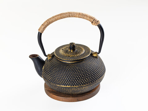 Asian cast iron teapot with black and gold dotted texture, rope wrapped handle and wooden stand, isolated on white, traditional tea culture
