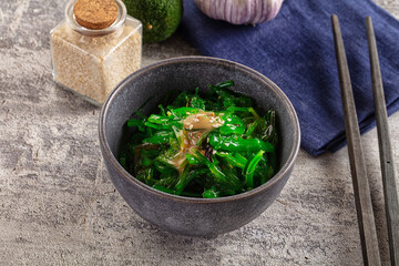 Japanese seaweed salad with sesame seeds and dressing in grey ceramic bowl on stone table with chopsticks © Andrei Starostin