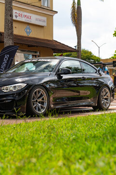 Black BMW M4 Sports Coupe Side Profile View Parked Near Urban Building Palm Tree Grass Foreground