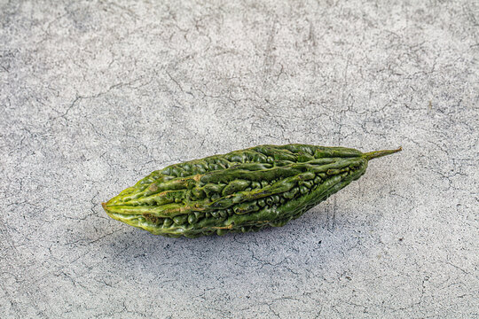 Gray textured surface with single green bitter melon showing wrinkled skin and tapered ends, food ingredient