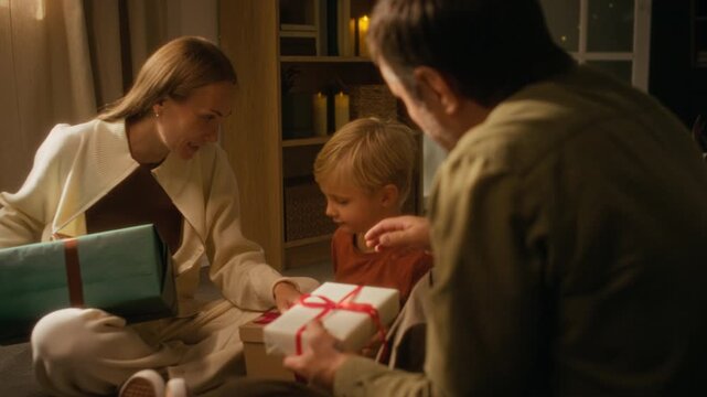 Middle aged Caucasian man giving wrapped presents to woman and son near Christmas tree. Visual fits festive holiday advertising and retail marketing campaigns