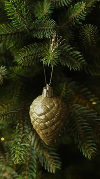 Vertical video. Female hands decorating Christmas tree, hanging golden Christmas ornaments.