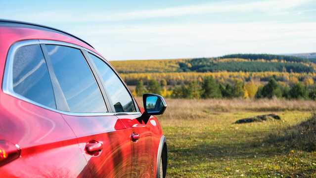 Red car side view parked in nature during autumn road trip, modern crossover vehicle with scenic forest background. Travel and adventure concept