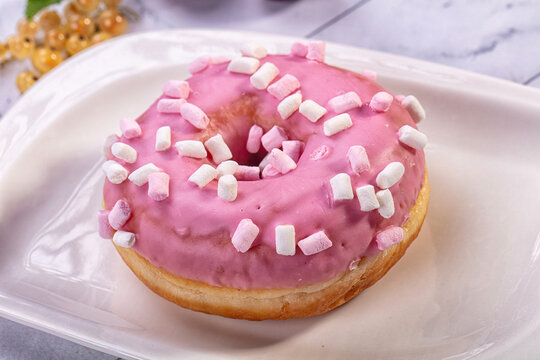 White ceramic plate holding glazed pastry topped with mini marshmallows and pink icing, baked sweet snack