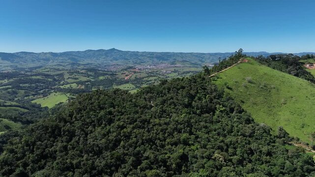 Vista a&eacute;rea de morro com mata e montanhas ao fundo