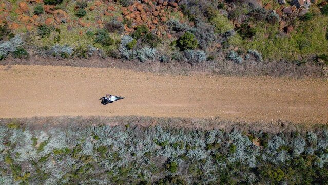 Aerial view of a motorcyclist riding on a gravel road through the natural landscape of Grabouw, Western Cape, South Africa.