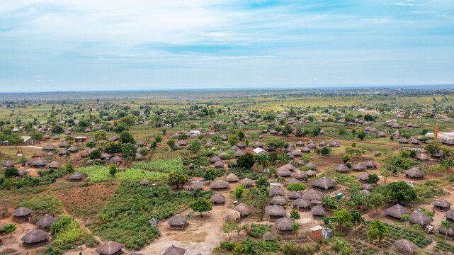 Aerial view of a rural village with numerous traditional thatched-roof huts, scattered trees, and cultivated agricultural plots in Yumbe, Northern Region, Uganda.