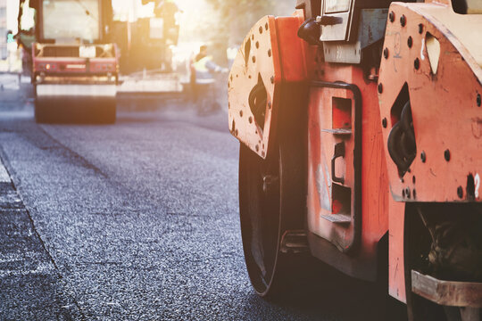 Road Roller Compacting Fresh Asphalt During City Street Paving in Metropolis. An orange road roller compacts fresh asphalt during city street paving in a metropolis.