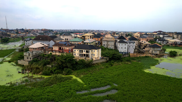 Aerial view of residential houses and buildings situated near a green, algae-covered waterway in Ojodu Berger, Lagos, Nigeria.