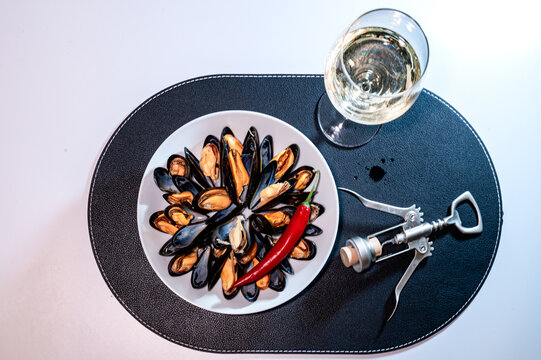 Seafood dinner table setting with steamed mussels white wine and a wing corkscrew on a black placemat. Ready-made layout with copy space for menus and gourmet evening concept.