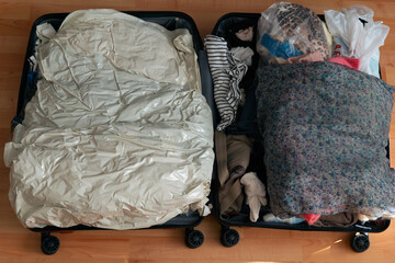 open suitcase packed with clothes and vacuum storage bags top view, both halves filled with folded garments on a wooden floor concept of travel, vacation, packing © Lana Pietukhova