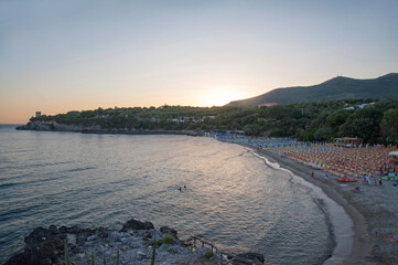 Calanca Beach, a sandy bay lined with beach umbrellas with hills and a historic turret on the cliff during evening dusk. Marina di Camerota, Salerno, Campania, Italy. © Tony