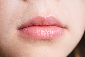 Obraz premium Close-up of natural pink lips with a glossy finish and slightly parted mouth. Detailed view of the lips, surrounding facial skin, and natural skin texture in soft lighting. Minimal makeup and realisti