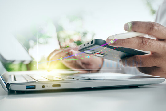 Businessman holding smartphone and stylus near laptop with digital financial trend line charts and data analytics overlay in outdoor setting, concept of business intelligence.