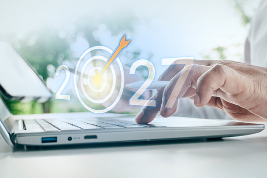 Businessman typing on laptop with digital target dartboard and year 2027 concept overlay in outdoor setting, concept of future business goal, strategic planning, and success.