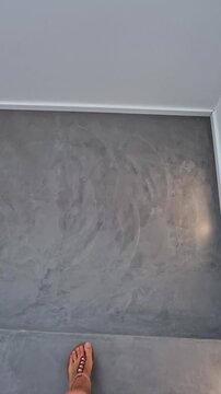 Low-angle point of view footage of feet walking down contemporary microcement stairs inside a minimalist residential interior, showcasing modern home design.