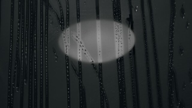 A steamed up hotel mirror with lamp reflection and dripping water droplets