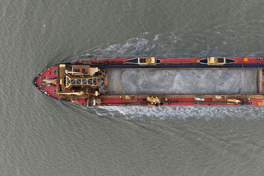 Aerial view of a large hopper dredger carrying a load of gravel through the water, leaving a wake, United Kingdom.