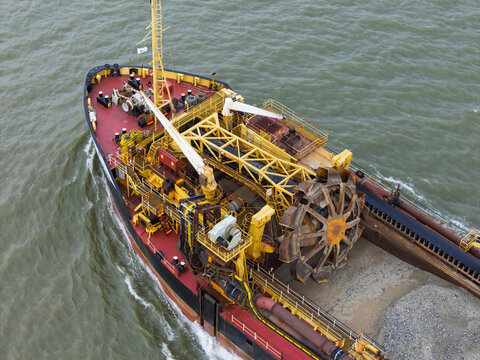 Aerial view of a large industrial dredger with a prominent rotating cutter wheel and yellow machinery on deck moving through the water in the United Kingdom.