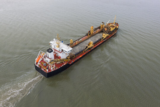Aerial view of a trailing suction hopper dredger ship moving through the water with industrial machinery on deck and a visible wake in the United Kingdom.