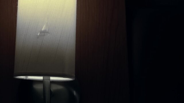 A broken hotel wall lamp being turned on in a dark, dingy room