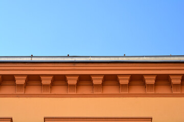 A low angle close up shot of decorative brown cornices and brackets supporting a roof line gutter under a clear blue sky. © nahhan