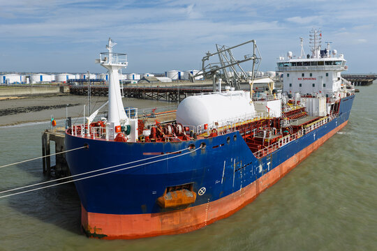 Aerial view of a large tanker ship docked at a terminal with white storage tanks visible in the background in the United Kingdom.