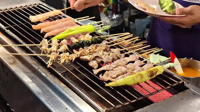 various thai style pork meat skewers and vegetables grilling on hot electric stove at local street food market stall