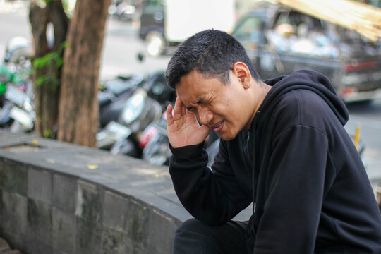 Asian man suffering from a headache, holding his head and feeling intense pain, against a bokeh background.