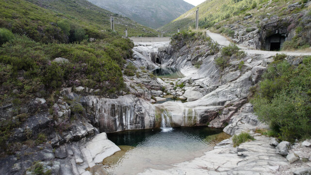 Aerial view of the natural rock pools at Pocos Verdes Sete Lagoas with a small waterfall and rugged mountain landscape in Cabril, Vila Real, Portugal.