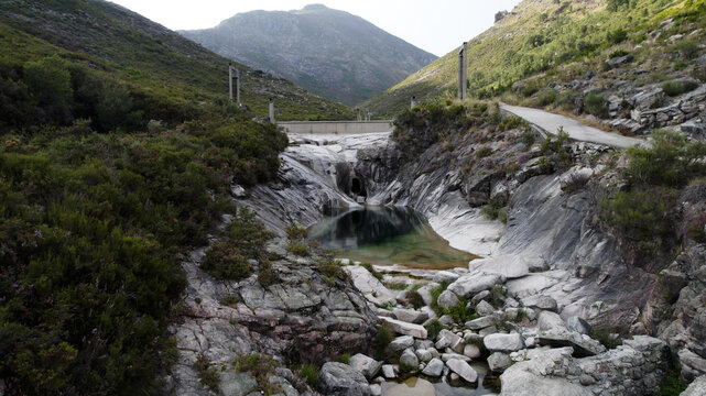 Aerial view of the natural pool at Pocos Verdes surrounded by rocky terrain, lush mountain vegetation, and a small dam structure in Cabril, Vila Real, Portugal.