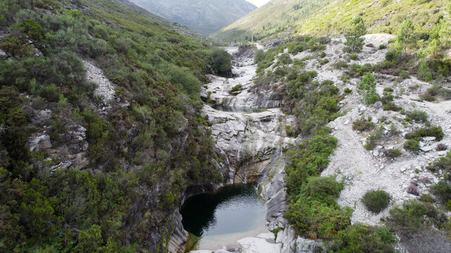Aerial view of the natural rock pools of Pocos Verdes in a rocky valley surrounded by lush green vegetation and hills in Cabril, Vila Real, Portugal.