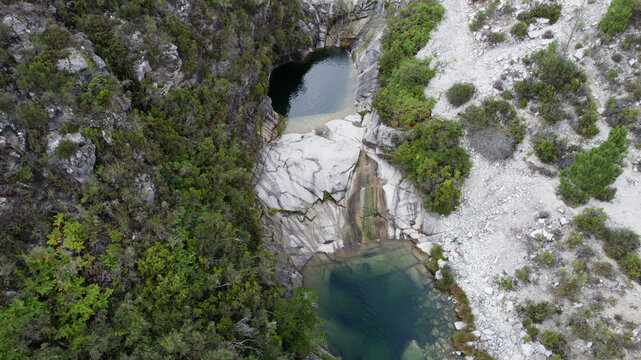 Aerial view of the Pocos Verdes natural pools and waterfall surrounded by rocky terrain and dense forest in Cabril, Vila Real, Portugal.
